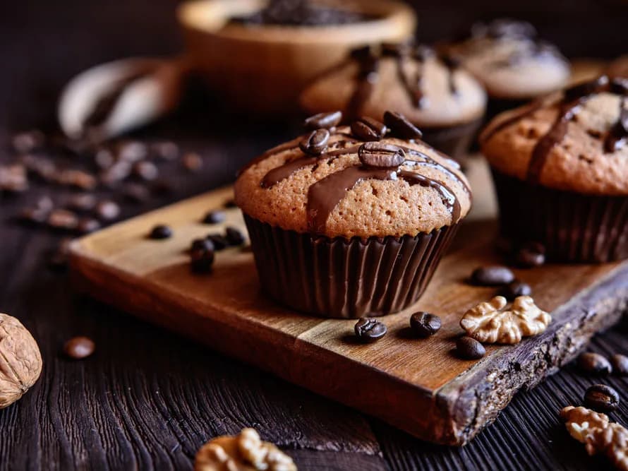 Muffins de chocolate cobertos com grãos de café e nozes, sobre uma tábua de madeira